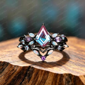 Könnte beinhalten: Ein Ring aus schwarzem Metall mit einem zentralen, drachenförmigen, irisierenden Stein, akzentuiert durch marquise-geschliffene Opale, runde violette Amethyste und kleine hellblaue Steine in einem chevron-förmigen Banddesign.