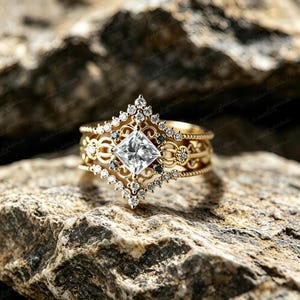 Peut inclure: Une bague en or avec une pierre centrale transparente taille princesse, entourée d'un halo géométrique de petites pierres transparentes rondes et de minuscules pierres noires. L'anneau présente un travail de filigrane et un motif perlé.
