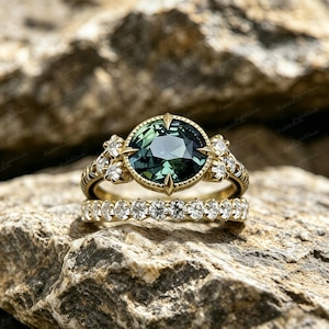 Puede incluir: Un juego de anillos de oro de dos piezas. El anillo de compromiso presenta una gema grande, redonda, de color verde azulado con un diseño de estrella. La banda está adornada con pequeños diamantes. La alianza es una banda de oro con una fila de pequeños diamantes.
