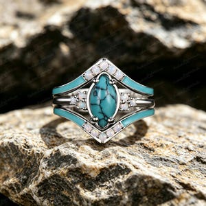 Könnte beinhalten: Ein dreiteiliges Ring-Set mit einem zentralen Türkisstein und weißen Akzentsteinen. Die Ringe haben ein silbernes Band und türkisfarbene Emaille-Details. Das Set wird auf einer strukturierten Felsfläche präsentiert.