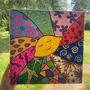May include: A colorful canvas painting with a smiling yellow lemon in the center. The lemon is surrounded by different patterns and designs, including circles, swirls, hearts, flowers, leaves, and geometric shapes.