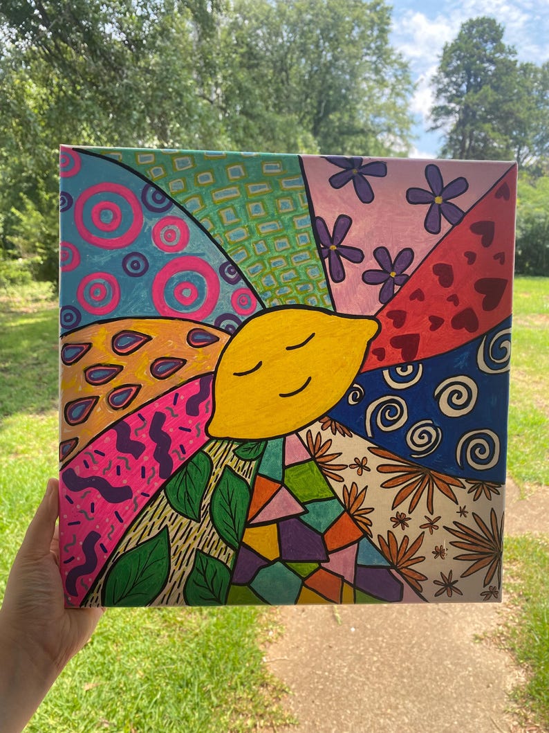 May include: A colorful canvas painting with a smiling yellow lemon in the center. The lemon is surrounded by different patterns and designs, including circles, swirls, hearts, flowers, leaves, and geometric shapes.