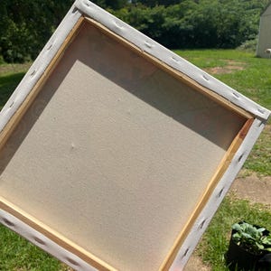 May include: The back of a blank canvas stretched over a wooden frame. The canvas is white and the frame is a light brown wood.