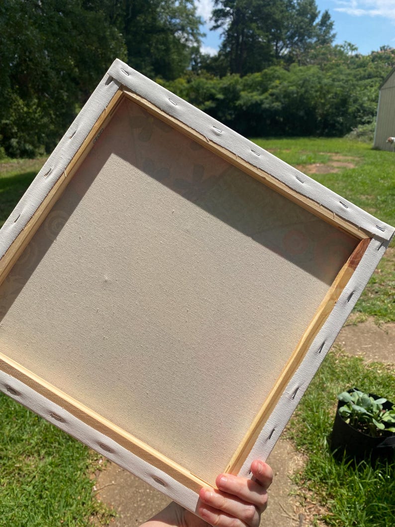 May include: The back of a blank canvas stretched over a wooden frame. The canvas is white and the frame is a light brown wood.