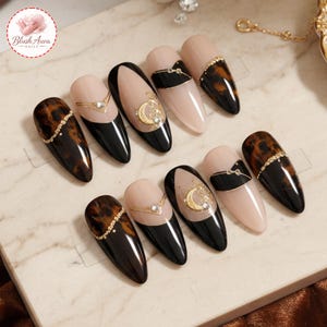 Peut inclure: Une collection de faux ongles en forme d'amande avec divers motifs. Certains ongles présentent un motif écaille de tortue, tandis que d'autres ont des pointes noires, des bases nude et des accents dorés. Certains ongles ont un motif de croissant de lune doré.