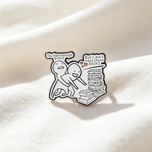 Può includere: Una spilla in smalto bianco e nero con due personaggi dei cartoni animati e una pila di libri. Un personaggio dice "You have enough BOOKS" mentre l'altro dice "But I don't have these BOOKS". La spilla è posta su uno sfondo bianco.