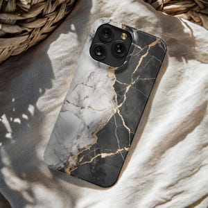 May include: A smartphone case with a marble design. The case features a split design with white and black marble, accented with gold-colored veining. The phone case has a black camera module with three lenses.