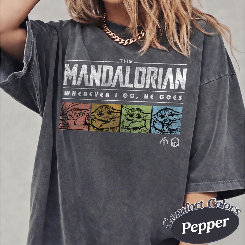 May include: Dark grey t-shirt featuring the text "THE MANDALORIAN" and "WHEREVER I GO, HE GOES." The shirt has a graphic of Baby Yoda in four colored squares. The shirt is a Comfort Colors Pepper.