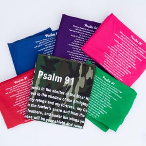May include: A selection of fabric squares in shades of blue, purple, pink, green, red, and camouflage, all bearing the text "Psalm 91" and a passage. The text is printed in white. The squares are arranged in a pile.