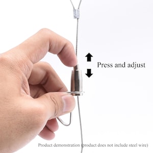 May include: A close-up of a metal cable hanging system. The text "Press and adjust" is next to the metal piece. The product demonstration text is at the bottom. The system is designed to be adjusted.