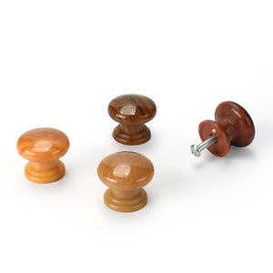 May include: Four wooden cabinet knobs in shades of brown and tan. Three knobs are mushroom-shaped, while one has a screw attached. The knobs have a glossy finish and are set against a white background.