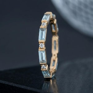 Può includere: Un anello a fascia in oro con un motivo alternato di pietre preziose azzurre taglio baguette e piccole pietre rotonde trasparenti. L'anello è montato su una struttura in oro giallo e presenta un design continuo lungo tutta la circonferenza.