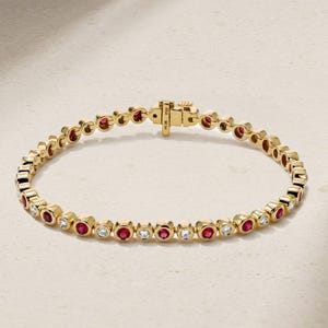Peut inclure: Un bracelet tennis en or orné d'une alternance de rubis rouges ronds et de diamants blancs transparents sertis clos. Le bracelet est composé de maillons circulaires individuels et comprend un fermoir à cliquet sécurisé avec un loquet de sûreté.
