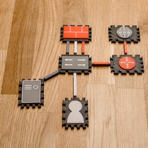 May include: A network diagram made of interlocking black, gray, and red pieces. The diagram includes a firewall, router, and a globe icon, all connected by lines. The pieces are on a wooden surface.