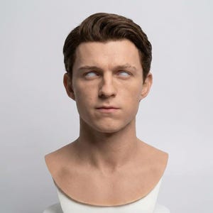 Pu&ograve; includere: Una scultura realistica di una testa umana con capelli castani corti pettinati con la riga laterale. I tratti del viso sono dettagliati con un'espressione neutra e gli occhi sono bianco solido senza pupille o iridi. Il busto &egrave; su una base.