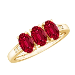 Op de afbeelding: Een geelgouden ring met drie ovaal geslepen dieprode robijnen op een rij. De ringband is aan weerszijden van de centrale stenen geaccentueerd met twee kleine, heldere, rond geslepen diamanten, vastgezet met gouden pootjes op een gepolijste band.