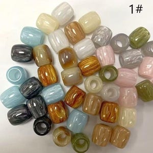 May include: A collection of barrel-shaped beads in various colors including blue, gray, pink, green, white, and amber. Each bead features a smooth, polished finish with a marbled or solid appearance and a central hole. The text 1# is visible.