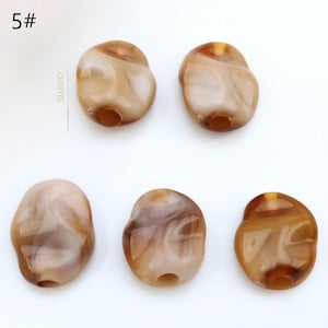 Pode incluir: Cinco contas de formato irregular com aparência marmorizada em tons de castanho e creme. Cada conta tem um furo para enfiar. O texto "5#" está no canto superior esquerdo.