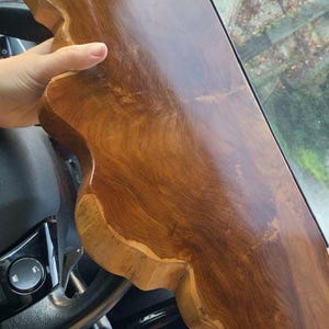 Pode incluir: Uma t&aacute;bua de madeira de bordo natural, polida, com uma forma irregular e um acabamento liso e brilhante. A madeira apresenta uma cor castanha quente e rica com padr&otilde;es de veios vis&iacute;veis e bordos org&acirc;nicos ondulados na lateral.