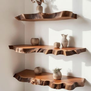 Pode incluir: Tr&ecirc;s prateleiras de parede feitas de placas de madeira natural com bordas brutas. As prateleiras est&atilde;o dispostas verticalmente num canto, apresentando um gr&atilde;o castanho rico. V&aacute;rios pequenos recipientes decorativos texturizados e de tons neutros est&atilde;o colocados sobre as superf&iacute;cies.