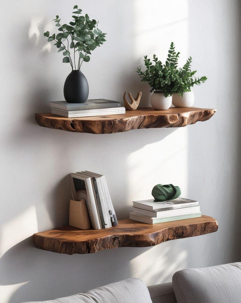 Pode incluir: Duas prateleiras horizontais montadas na parede feitas de madeira natural com bordas irregulares. A prateleira superior cont&eacute;m uma pilha de livros, um vaso preto com folhagem verde, uma pequena escultura de madeira e dois vasos brancos.