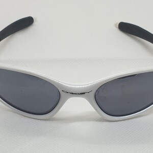 Puede incluir: Gafas de sol blancas con lentes grises oscuras y puntas de patillas negras. Las gafas de sol tienen un dise&ntilde;o elegante y moderno, con el nombre de la marca sutilmente mostrado en la montura.