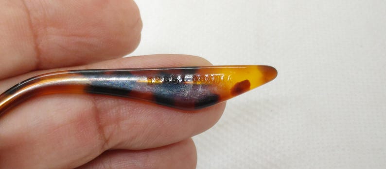 May include: Close-up of a tortoiseshell-patterned eyeglass arm. The arm is a mix of brown, black, and amber colors. The text "120/50/140" is printed on the arm.