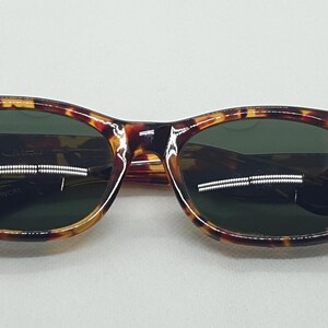 Puede incluir: Gafas de sol con montura de carey y lentes verde oscuro. Las monturas tienen una forma redondeada cl&aacute;sica con un patr&oacute;n moteado marr&oacute;n y &aacute;mbar. Las lentes son de color verde oscuro, contrastando con la montura.