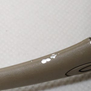Puede incluir: Primer plano de un objeto curvo de color topo con un dise&ntilde;o circular y un peque&ntilde;o agujero. La superficie muestra zonas con pintura descascarillada, revelando un color m&aacute;s claro debajo. La forma del objeto sugiere que podr&iacute;a ser parte de un elemento m&aacute;s grande.