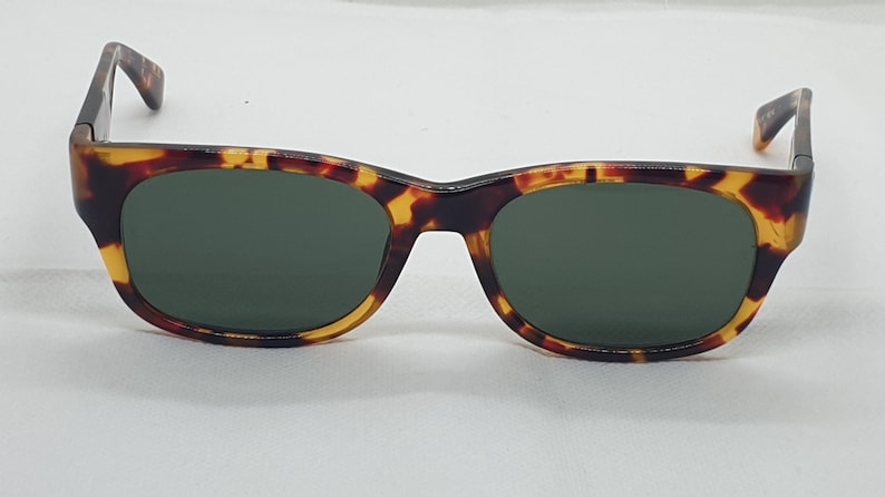 Puede incluir: Gafas de sol con montura con estampado de carey y lentes verde oscuro. Las gafas de sol tienen una forma rectangular cl&aacute;sica con una l&iacute;nea de cejas ligeramente curvada. Las patillas son de color marr&oacute;n oscuro.
