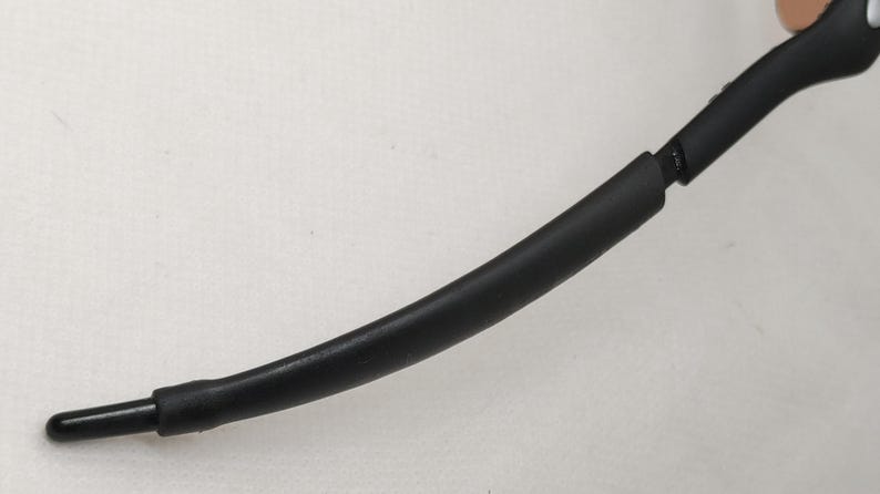 May include: A black eyeglass arm with a curved design. The arm is made of a smooth, matte material and has a rounded tip. The arm is connected to a hinge.