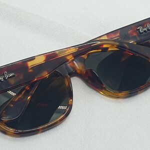 Puede incluir: Gafas de sol carey con lentes oscuras. Las monturas tienen un patr&oacute;n marr&oacute;n y amarillo. El logotipo de Ray-Ban es visible en las patillas. Las gafas de sol est&aacute;n plegadas.