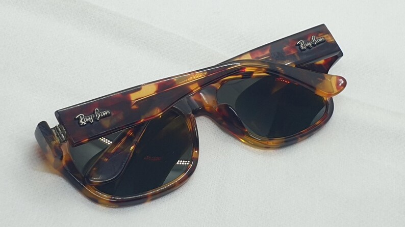 Puede incluir: Gafas de sol carey con lentes oscuras. Las monturas tienen un patr&oacute;n marr&oacute;n y amarillo. El logotipo de Ray-Ban es visible en las patillas. Las gafas de sol est&aacute;n plegadas.