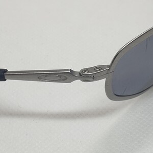 K&ouml;nnte beinhalten: Nahaufnahme einer Sonnenbrille mit silbernem Metallrahmen und blau get&ouml;nten Gl&auml;sern. Die B&uuml;gel haben eine dunkelblaue Gummiummantelung. Die Brille dient dem Sonnenschutz.