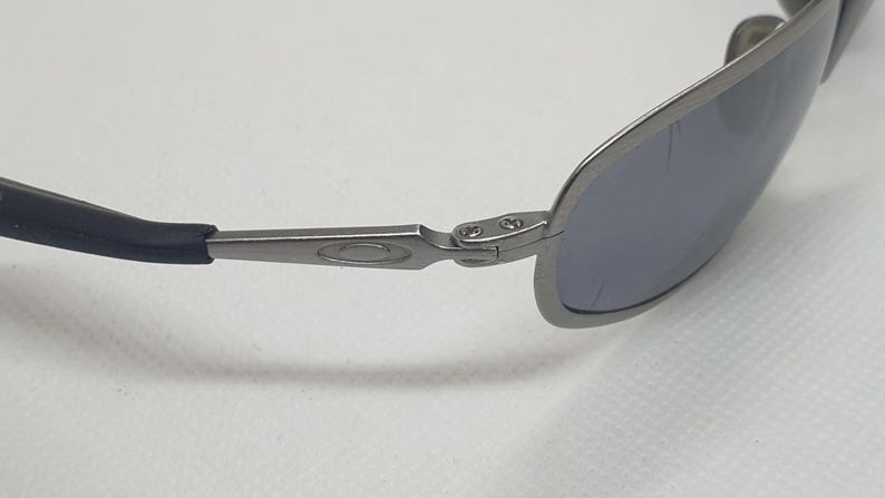 K&ouml;nnte beinhalten: Nahaufnahme einer Sonnenbrille mit silbernem Metallrahmen und blau get&ouml;nten Gl&auml;sern. Die B&uuml;gel haben eine dunkelblaue Gummiummantelung. Die Brille dient dem Sonnenschutz.