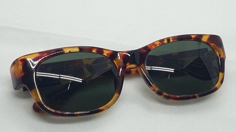 Puede incluir: Gafas de sol carey con lentes verde oscuro. Las monturas presentan un patr&oacute;n cl&aacute;sico de marr&oacute;n, &aacute;mbar y negro. Estas gafas de sol son un accesorio elegante para la protecci&oacute;n de los ojos del sol.