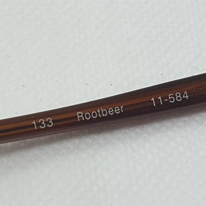 Pode incluir: Close-up de uma haste de &oacute;culos castanha com o texto "Rootbeer", "133" e "11-584" impresso. A haste &eacute; de cor castanho escuro.
