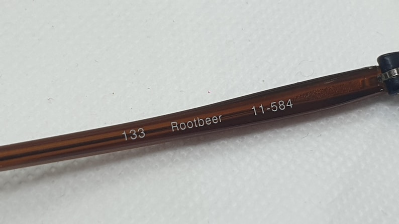 Pode incluir: Close-up de uma haste de &oacute;culos castanha com o texto "Rootbeer", "133" e "11-584" impresso. A haste &eacute; de cor castanho escuro.