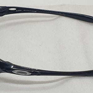 Puede incluir: Gafas de sol negras con montura curvada y lentes oscuras. Las gafas de sol tienen un dise&ntilde;o elegante y moderno con un peque&ntilde;o emblema plateado en el lateral de la montura. Las patillas son largas y ligeramente curvadas.