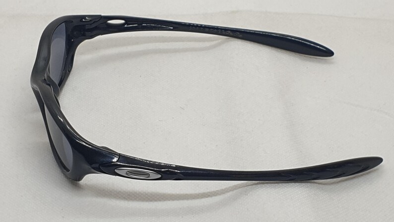 Puede incluir: Gafas de sol negras con montura curvada y lentes oscuras. Las gafas de sol tienen un dise&ntilde;o elegante y moderno con un peque&ntilde;o emblema plateado en el lateral de la montura. Las patillas son largas y ligeramente curvadas.