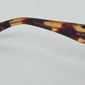 Puede incluir: Primer plano de una patilla de gafas con estampado de carey. La patilla se curva suavemente y presenta el texto "WCAL" y "BOHEMIAN". La paleta de colores incluye tonos marrones, &aacute;mbar y negro.