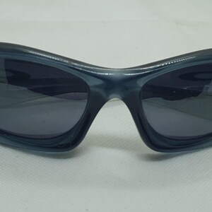 May include: Dark blue sunglasses with a curved, wraparound design. The lenses are a darker shade of blue, providing a sleek and modern look. These sunglasses offer a sporty aesthetic.