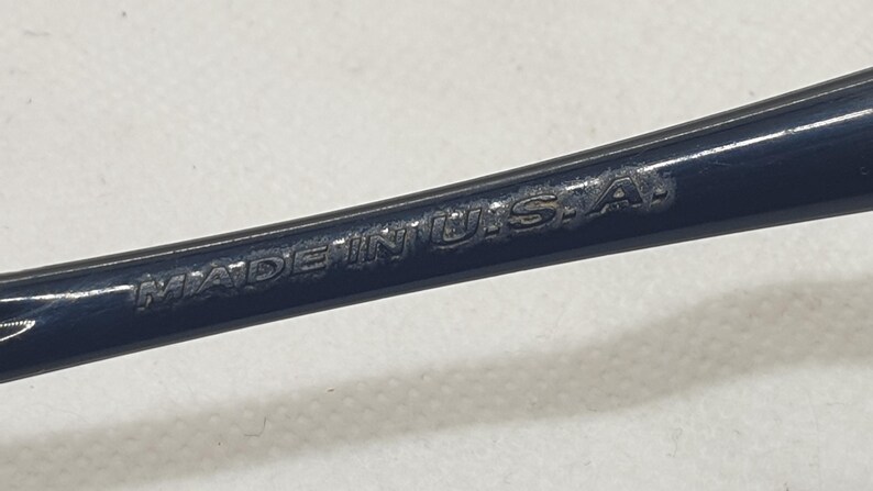 Puede incluir: Primer plano de un objeto met&aacute;lico azul oscuro con el texto "MADE IN U.S.A." grabado en la superficie. El texto est&aacute; en may&uacute;sculas y parece ligeramente desgastado.