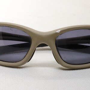 Puede incluir: Gafas de sol ovaladas con montura beige y lentes gris oscuro. Las gafas tienen un dise&ntilde;o elegante y curvado y son adecuadas para actividades al aire libre. Las lentes protegen del deslumbramiento solar.