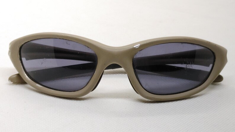 Puede incluir: Gafas de sol ovaladas con montura beige y lentes gris oscuro. Las gafas tienen un dise&ntilde;o elegante y curvado y son adecuadas para actividades al aire libre. Las lentes protegen del deslumbramiento solar.