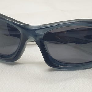 May include: Dark blue sunglasses with a curved, wraparound design. The lenses are dark, and the frames have a glossy finish. These sunglasses offer a sporty, modern look.