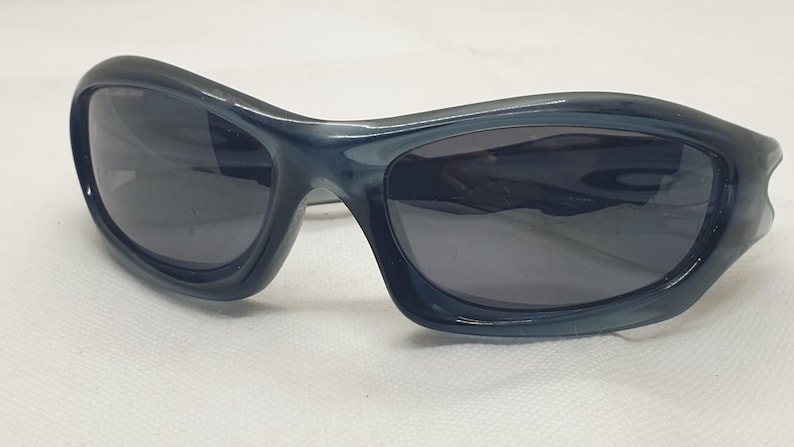 May include: Dark blue sunglasses with a curved, wraparound design. The lenses are dark, and the frames have a glossy finish. These sunglasses offer a sporty, modern look.