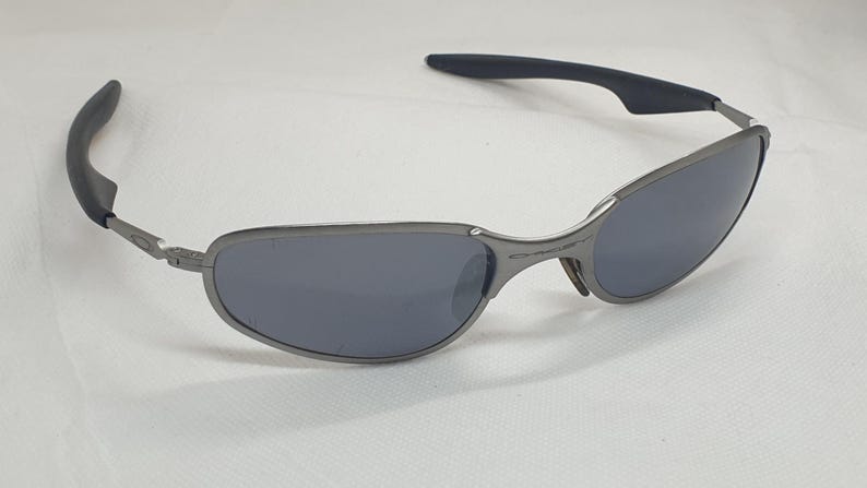 K&ouml;nnte beinhalten: Graue Sonnenbrille mit dunklen Gl&auml;sern. Die Fassungen sind metallisch grau, und die B&uuml;gel haben schwarze Gummigriffe. Die Gl&auml;ser sind dunkelgrau und bieten Sonnenschutz.