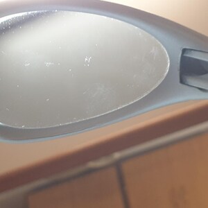 K&ouml;nnte beinhalten: Nahaufnahme einer grauen Sonnenbrille. Die ovalen Gl&auml;ser sind in einem matten grauen Rahmen gefasst. Die Sonnenbrille ist abgewinkelt, wodurch Details von Rahmen und Gl&auml;sern sichtbar werden.