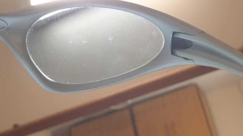 K&ouml;nnte beinhalten: Nahaufnahme einer grauen Sonnenbrille. Die ovalen Gl&auml;ser sind in einem matten grauen Rahmen gefasst. Die Sonnenbrille ist abgewinkelt, wodurch Details von Rahmen und Gl&auml;sern sichtbar werden.